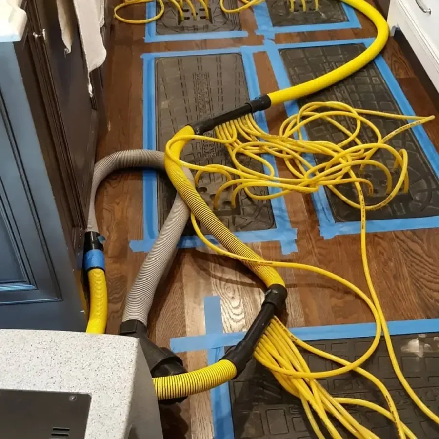 Drying mats laid across a hardwood floor with yellow hoses running to a drying machine