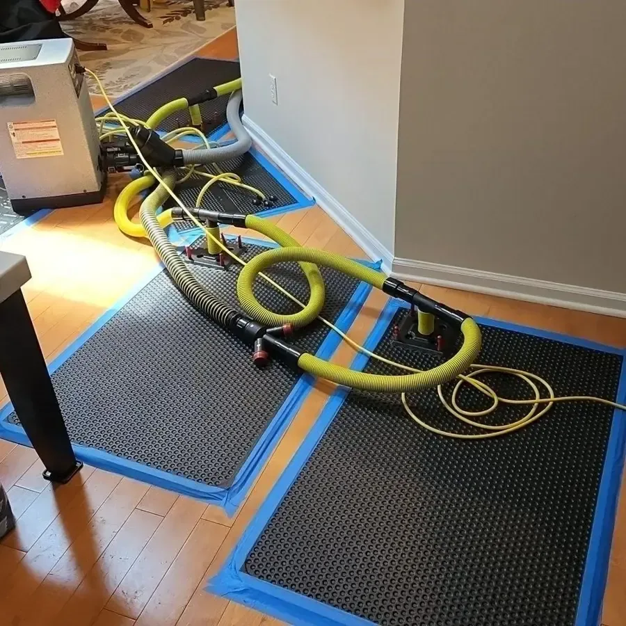 Black drying mats taped over a wood floor with yellow hoses and a drying machine